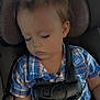 child, toddler, sleeping, car_seat, car, harness, plaid_shirt, blue_shirt, orange_shirt, seatbelt, young_child, closed_eyes, hair, skin, interior, safety, rest, peaceful, casual_clothing, portrait