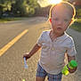 child, toddler, road, sunlight, bubble_solution, bubble_wand, shorts, shirt, shoes, outdoor, summer, daylight, sunflare, portrait, playing, young_child, casual_clothing, nature, greenery, sidewalk