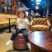 Ousseid Kais joined the competition — help win amazing prizes! armchair, bookshelves, booth, cafe, casual_clothing, child, family_outing, indoors, interior_design, leather_furniture, pendant_lights, plants, portrait, restaurant, seated, smiling, sneakers, table, thumbs_up, toddler