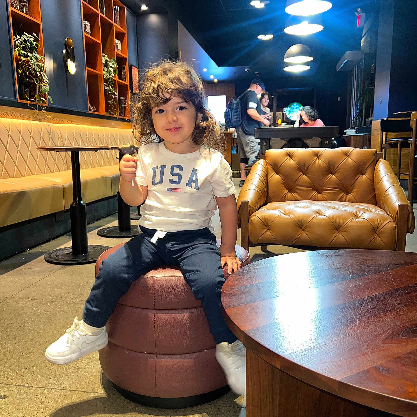 Ousseid Kais joined the competition — help win amazing prizes! armchair, bookshelves, booth, cafe, casual_clothing, child, family_outing, indoors, interior_design, leather_furniture, pendant_lights, plants, portrait, restaurant, seated, smiling, sneakers, table, thumbs_up, toddler
