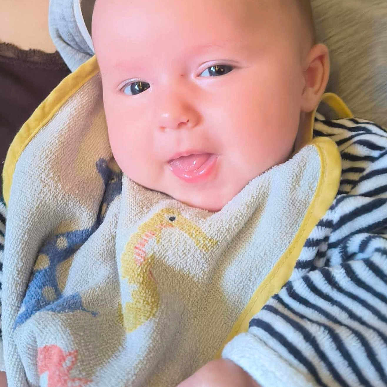 Maéna participe au concours pour gagner de l'argent avec cette photo : baby, bib, cheeks, child, closeup, clothing, cute, expression, eyes, fabric, face, hand, holding, infant, person, portrait, skin, smiling, striped_clothing, tongue