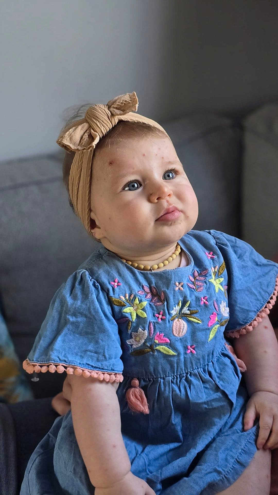 Jeanne participe au concours pour gagner de l'argent avec cette photo : baby, child, blue_dress, headband, bow, embroidery, flowers, couch, indoors, portrait, cute, infant, sitting, person, face, skin, expression, happy, necklace, soft_lighting