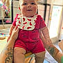 baby, bib, child, chubby, curious_toddler, cute, face, hand, holding, indoor, infant, kitchen, light, person, red_clothing, shorts, smile, table, tattoo, window