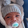 baby, pacifier, hat, knitted_hat, pom_poms, jacket, fur_lining, close_up, face, infant, cute, warm_clothing, child, portrait, expression, newborn, soft_texture, winter_wear, adorable, love