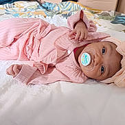 Romy participe au concours pour gagner de l'argent avec cette photo : baby, infant, pacifier, pink_clothing, headband, bow, blanket, bed, soft_texture, lying_down, cute, child, indoors, person, sleepwear, comfortable, toddler, portrait, young_child, resting