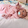 baby, infant, pacifier, pink_clothing, headband, bow, blanket, bed, soft_texture, lying_down, cute, child, indoors, person, sleepwear, comfortable, toddler, portrait, young_child, resting