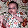 baby, infant, face, hands, onesie, floral_pattern, bedspread, flower_pattern, skin, person, cute, lying_down, expression, clothing, child, newborn, closeup, indoor, portrait, human