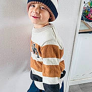 Sacha a rejoint le concours — aidez-le/la à gagner de superbes lots ! child, boy, smiling, indoor, striped_sweater, knit_hat, socks, wooden_floor, playful, standing, casual, home, person, portrait, happy, clothing, floor, wall, cozy, cute