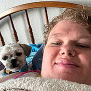 Evee is registered to the contest to win money with this photo: person, dog, bed, blanket, headboard, indoor, portrait, closeup, curly_hair, white_wall, resting, comfort, cute, pet, animal, cozy, relaxed, smile, fur, wood