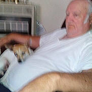 Isabella joined the competition — help win amazing prizes! elderly_man, dog, indoor, chair, relaxing, white_shirt, pet, home, furniture, human, animal, resting, blurred, hand, clock, remote_control, casual, seated, living_room, comfort