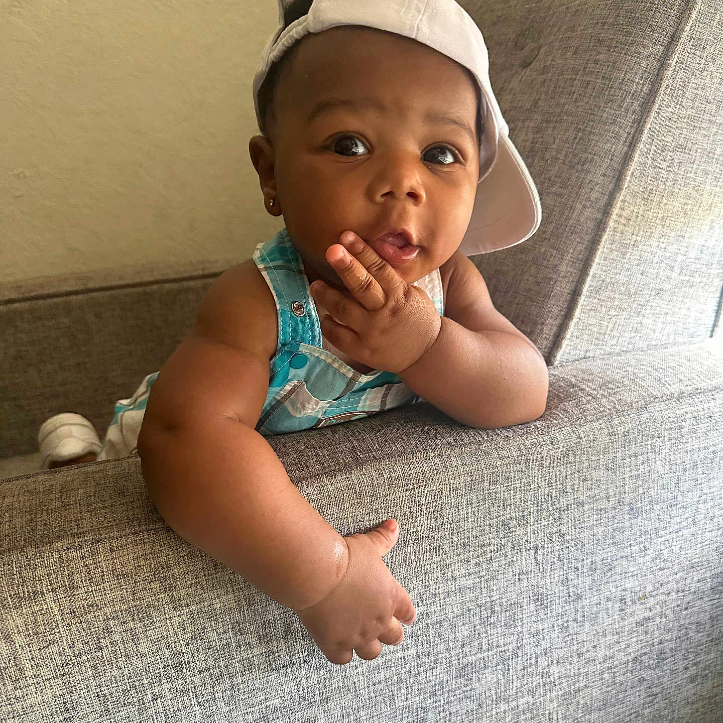 Makhai is registered to the contest to win money with this photo: baby, cap, child, clothing, couch, curious, cute, expression, face, furniture, hand, hat, indoor, infant, overalls, person, portrait, seat, skin, young