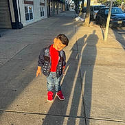 Krishiv is registered to the contest to win money with this photo: child, boy, smiling, outdoor, sidewalk, street, urban, portrait, standing, fashion, jacket, red_shirt, jeans, sneakers, red_shoes, parked_cars, storefronts, trees, shadows, dog_waste_sign
