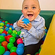 Riley is registered to the contest to win money with this photo: baby, child, ball_pit, blue_ball, colorful_balls, happy, smiling, blue_eyes, light_blue_shirt, dark_pants, indoor, playtime, cute, small_hands, joyful, seated, toy, fun, infant, playground