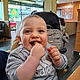 baby, child, smiling, eating, indoor, restaurant, high_chair, clothing, face, hand, food, table, bag, stroller, happy, person, apparel, sitting, infant, casual