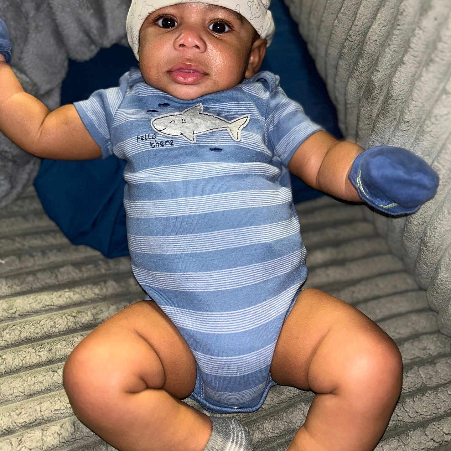 Phoenix is registered to the contest to win money with this photo: baby, infant, child, onesie, hat, mitten, socks, blue, striped, plush_blanket, couch, curious, face, legs, arms, cute, indoor, portrait, person, cozy