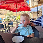 Nino participe au concours pour gagner de l'argent avec cette photo : child, boy, blond, espresso, cup, cafe, outdoor, table, chair, tattoo, red_umbrella, daylight, clothing, person, drink, plate, casual, curious, blue_eyes, short_sleeves