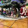Jules a rejoint le concours — aidez-le/la à gagner de superbes lots ! cat, christmas_tree, holiday_decorations, santa_figurine, nativity_scene, ornaments, snowman_figurine, tinsel, christmas_lights, floor_tiles, festive, indoors, holiday, gray_cat, pine_cones, gift_box, christmas_spirit, decoration, curious_cat, festive_scene