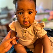 Azlyn joined the competition — help win amazing prizes! baby, infant, child, person, hand, skin, face, eyes, mouth, clothing, beige, indoor, blurred_background, sitting, feet, cute, expression, holding, young, portrait