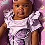 Azlyn is registered to the contest to win money with this photo: apparel, baby, bow, child, closeup, curly_hair, cushion, cute, face, headband, indoor, infant, pattern, person, portrait, purple_clothing, sitting, smile, soft_lighting, unicorn