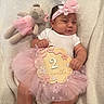 baby, infant, pink_tutu, headband, flower, plush_toy, teddy_bear, blanket, milestone_sign, smiling, cute, lying_down, soft_texture, white_clothing, decorative_sign, child, portrait, indoor, adorable, two_months