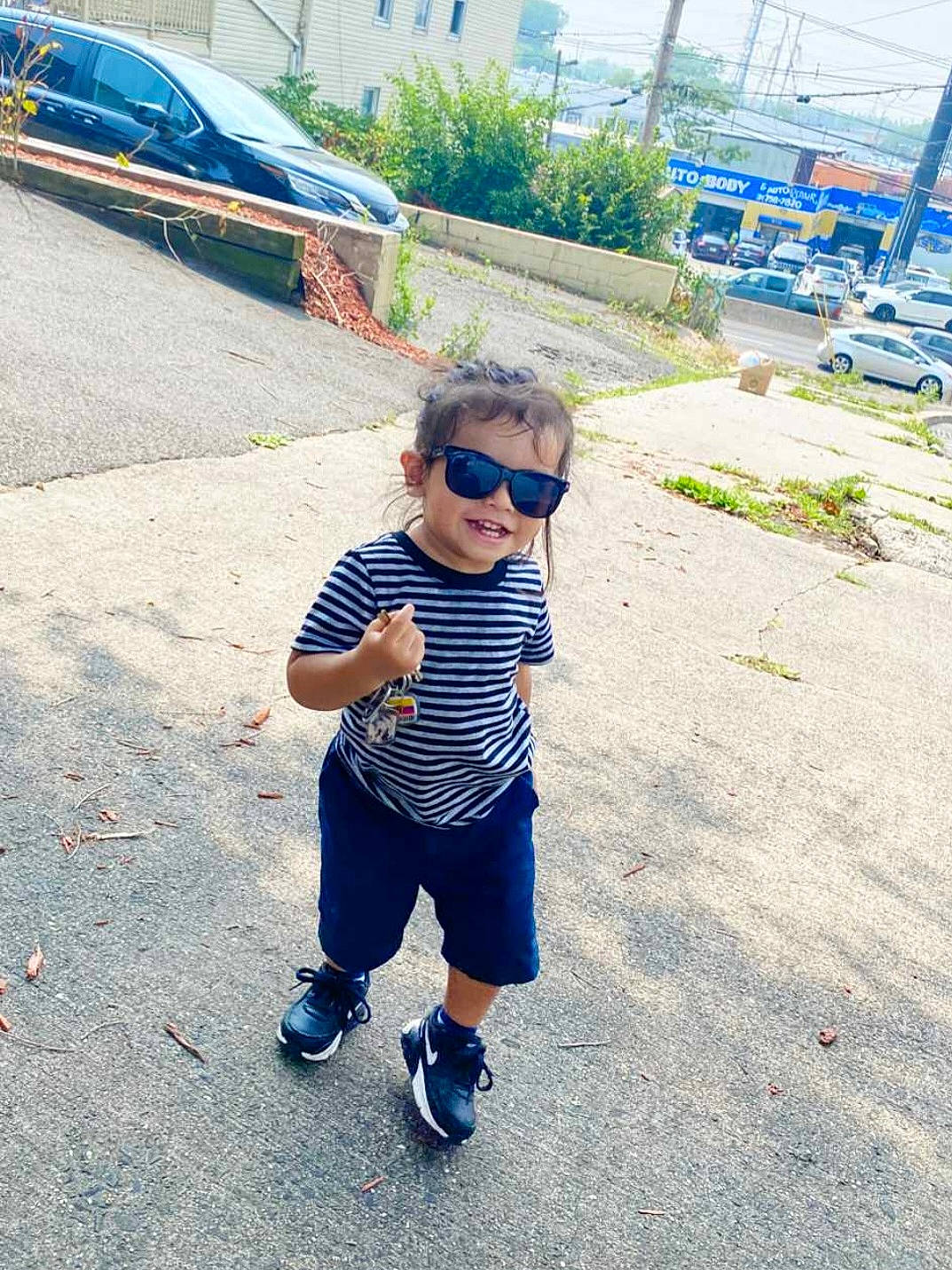 Ethan is registered to the contest to win money with this photo: asphalt, automotive_lighting, car, cool, electric_blue, eyewear, fun, glasses, grass, leisure, person, plant, recreation, road_surface, shorts, sidewalk, sunglasses, t_shirt, toddler, tree