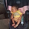baby, infant, sleeping, car_seat, bottle, yellow_clothing, pink, black, curly_hair, indoors, couch, cushion, peaceful, child, person, footwear, bracelet, resting, toddler, young_child
