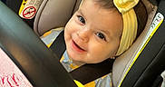 Izabella is registered to the contest to win money with this photo: baby, child, car_seat, yellow_bow, headband, smile, happy, infant, toy, blanket, seatbelt, closeup, indoor, cute, person, face, clothing, colorful, soft, safety