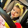 baby, child, car_seat, yellow_bow, headband, smile, happy, infant, toy, blanket, seatbelt, closeup, indoor, cute, person, face, clothing, colorful, soft, safety