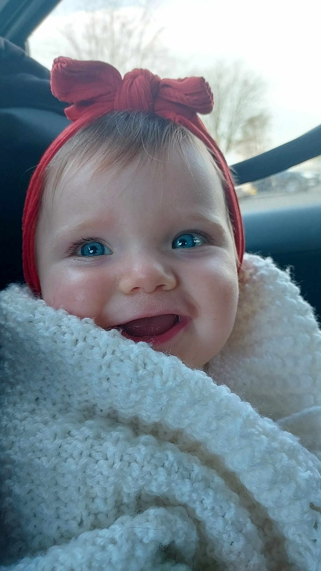 Caliopé a rejoint le concours — aidez-le/la à gagner de superbes lots ! baby, blanket, blue_eyes, bow, car_interior, child, closeup, cozy, cute, face, happy, headwear, infant, knit, person, portrait, red_headband, smiling, warm, young_child