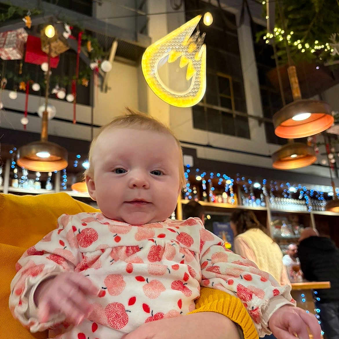 Zelie a rejoint le concours — aidez-le/la à gagner de superbes lots ! baby, background, casual, child, clothing, cozy, decorations, face, festive, hand, holding, indoor, infant, lights, onesie, pattern, people, person, restaurant, warm_lighting