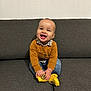 Leo a rejoint le concours — aidez-le/la à gagner de superbes lots ! baby, child, smiling, happy, sitting, couch, indoor, socks, yellow_socks, jeans, sweater, checkered_shirt, face, hands, feet, cozy, portrait, young_child, furniture, wall