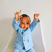 Devick joined the competition — help win amazing prizes! toddler, child, smiling, blue_suit, checkered_suit, raised_hands, white_chair, indoor, portrait, happy, cute, fashion, casual, person, young_child, baby_face, seated, celebration, joy, minimalist_background