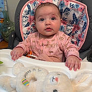 Lily joined the competition — help win amazing prizes! baby, child, high_chair, pink_clothing, plush_toy, bunny, face, blue_eyes, indoor, cushion, floral_pattern, hand, table, infant, cute, person, closeup, soft_toy, seated, curious