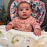 baby, child, high_chair, pink_clothing, plush_toy, bunny, face, blue_eyes, indoor, cushion, floral_pattern, hand, table, infant, cute, person, closeup, soft_toy, seated, curious