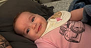 Lily joined the competition — help win amazing prizes! baby, child, smiling, pink_shirt, bib, blanket, tattoo, face, blue_blanket, bed, pillow, indoor, person, infant, cute, lying_down, monkey_design, car_print, relaxed, home