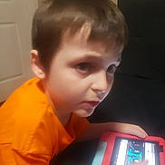 Sebastian joined the competition — help win amazing prizes! child, boy, tablet, orange_shirt, indoor, furniture, door, technology, screen, hand, focused, young, person, casual, playing, digital_device, seated, room, hair, skin