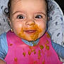 Delilah joined the competition — help win amazing prizes! baby, child, high_chair, bib, messy, food, orange_food, smiling, happy, curly_hair, brown_eyes, earrings, clothing, face, hand, indoor, portrait, cute, infant, feeding_time