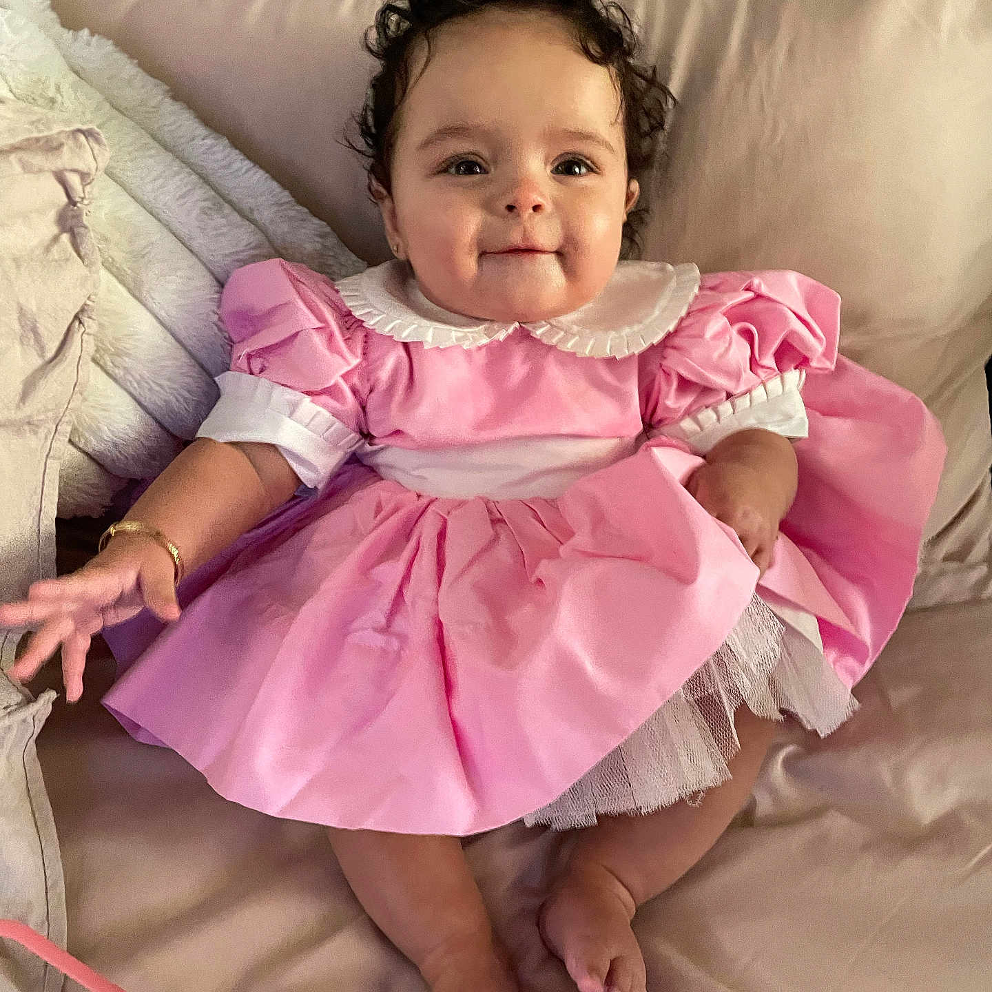 Delilah joined the competition — help win amazing prizes! baby, bed, bracelet, child, curly_hair, cute, fabric, feet, hand, happy, indoors, infant, pillow, pink_dress, portrait, sitting, skin, smile, soft_texture, tulle