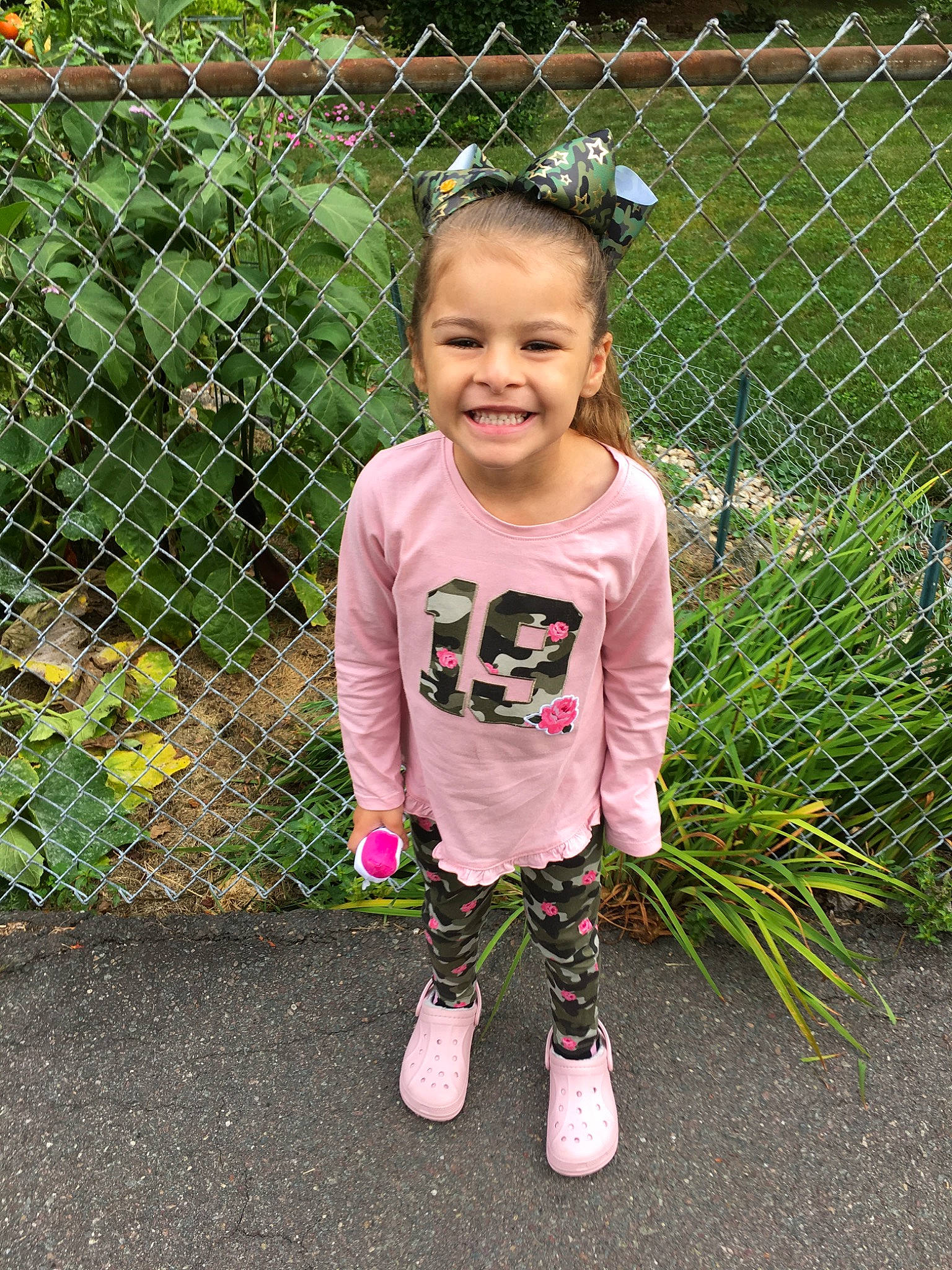 Aleena is registered to the contest to win money with this photo: baby_toddler_clothing, child, fence, footwear, garden, grass, hairstyle, happy, joy, net, pattern, person, pink, plant, play, shoe, skin, smile, t_shirt, toddler