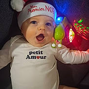Aaron a rejoint le concours — aidez-le/la à gagner de superbes lots ! baby, infant, child, santa_hat, christmas, holiday, onesie, text_clothing, toy, glowing, colorful_lights, face, expression, happy, cute, lying_down, indoor, closeup, portrait, festive