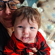 Bailey is registered to the contest to win money with this photo: baby, child, adult, glasses, tongue_out, red_clothing, checkered_pattern, indoor, portrait, smiling, face, hands, hair_bow, close_up, holding, person, happy, warm_lighting, family, cute