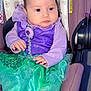 baby, child, car_seat, purple_clothing, green_skirt, costume, sparkle, face, hands, infant, seatbelt, floral_pattern, indoor, cute, looking_away, soft_lighting, clothing, fabric, portrait, person