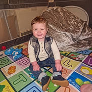 Lorenzo is registered to the contest to win money with this photo: toddler, child, smiling, indoor, playmat, alphabet, colorful, clothing, vest, jeans, shoes, blanket, plush, playpen, happy, sitting, toy, floor, person, home