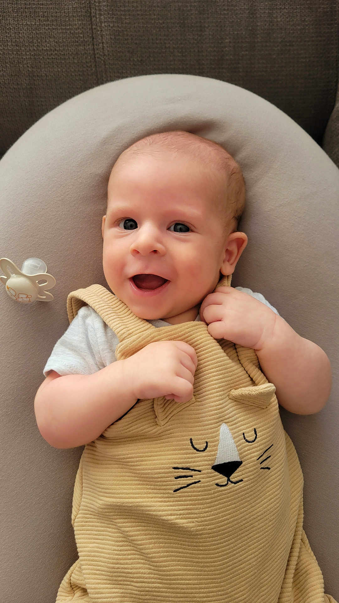 Estéban a rejoint le concours — aidez-le/la à gagner de superbes lots ! baby, infant, smiling, happy, cute, pacifier, beige_clothing, cat_design, cushion, soft_fabric, indoor, child, portrait, closeup, light_skin, short_hair, eyes, hands, relaxed, comfortable