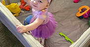 Raven is registered to the contest to win money with this photo: baby, ball, carpet, child, clothing, colorful, cute, fun, happy, headband, indoor, person, playing, playpen, purple, smiling, standing, toy, tutu, young