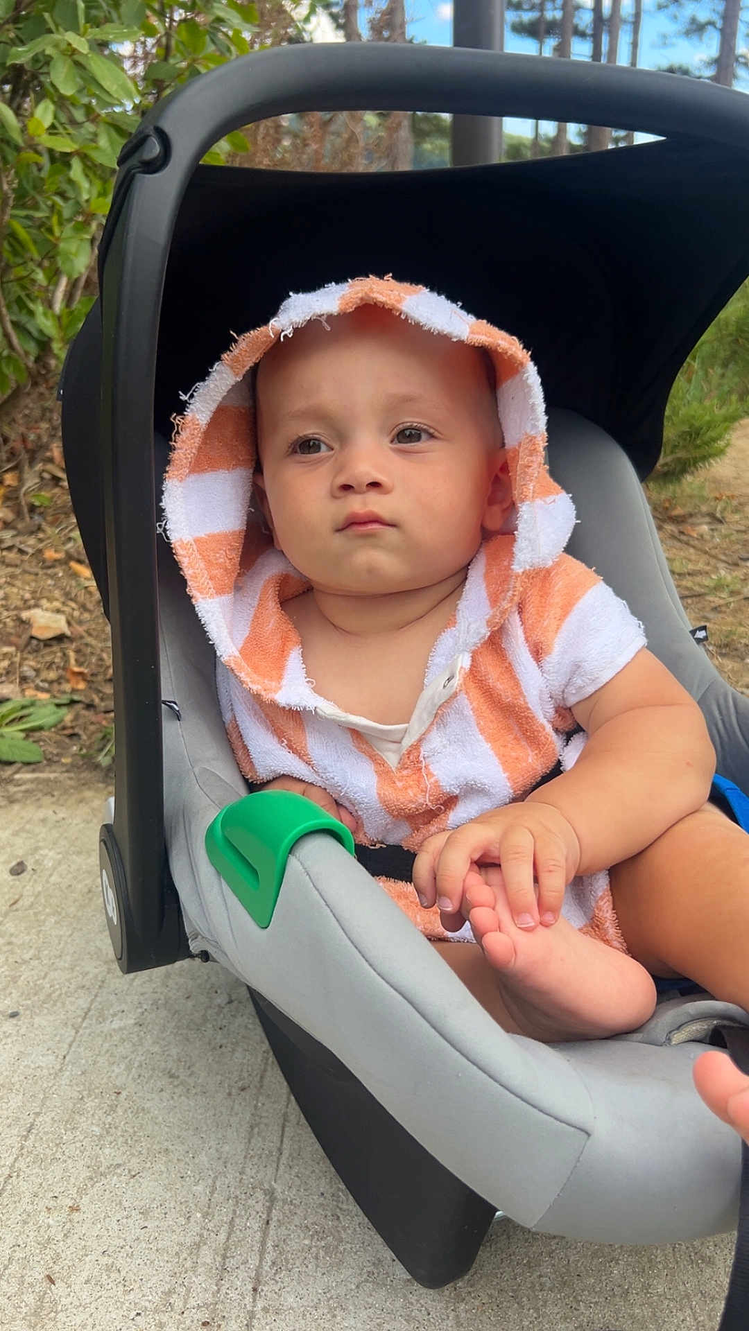 Aslan participe au concours pour gagner de l'argent avec cette photo : baby, child, car_seat, hooded_towel, orange_stripes, outdoor, sidewalk, greenery, hand, foot, curious, toddler, person, infant, seat, cute, casual, daylight, portrait, expression