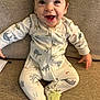 Remington is registered to the contest to win money with this photo: baby, child, smiling, onesie, animal_print, slippers, couch, indoor, happy, cute, infant, face, portrait, seated, young_child, cozy, clothing, expression, home, toddler