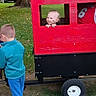 Justin is registered to the contest to win money with this photo: children, baby, toddler, outdoor, backyard, wagon, toy_vehicle, red, black, grass, trees, autumn, parked_truck, jersey, window, standing, peeking, playful, family, daylight