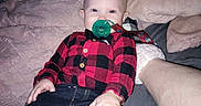 Justin is registered to the contest to win money with this photo: baby, bed, bedroom, black_clothing, blanket, blue_toy, checkered_shirt, child, cozy, face, indoors, infant, jeans, pacifier, pajamas, portrait, red_clothing, sitting, toy, wide_eyes