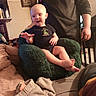 baby, child, infant, smiling, sitting, chair, plush_chair, adult, indoor, home, living_room, clothing, blanket, toys, furniture, portrait, barefoot, happy, family, cozy